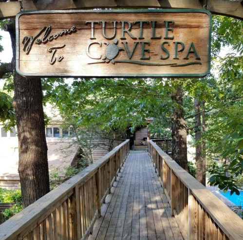 Wooden walkway leading to a sign that reads "Welcome to Turtle Cove Spa," surrounded by trees.