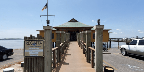 A wooden dock leads to a yellow building by the water, with an American flag and a sign for Regatta restaurant.
