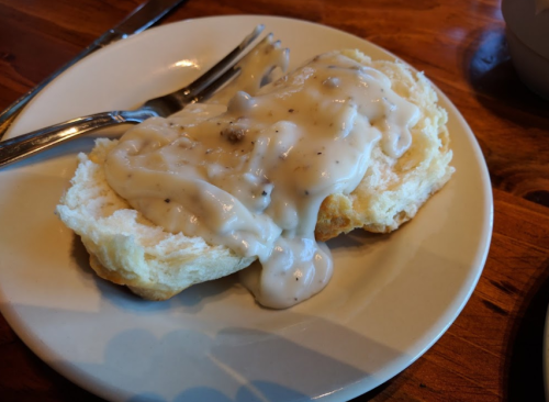 A plate with a biscuit topped with creamy sausage gravy, accompanied by a fork and knife.