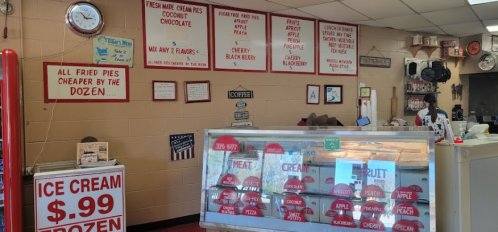 A cozy shop interior with signs for pies, ice cream, and meats, featuring a display case and a wall clock.
