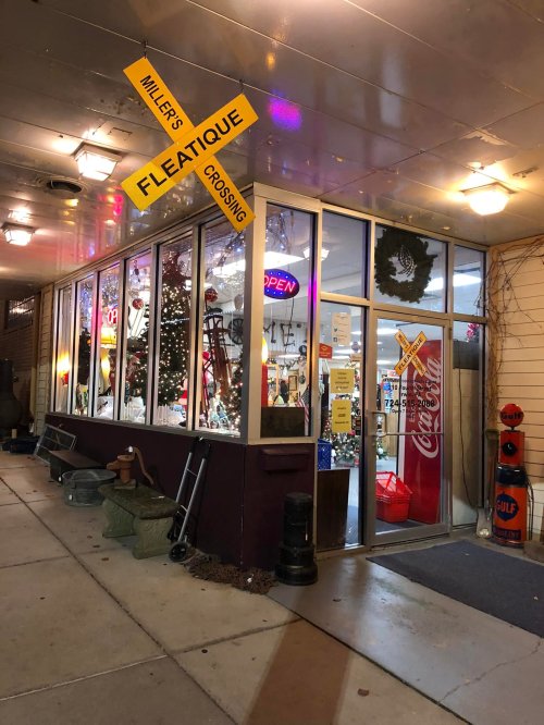 A storefront with a sign reading "Miller's Fleatique Crossing," featuring colorful lights and holiday decorations.