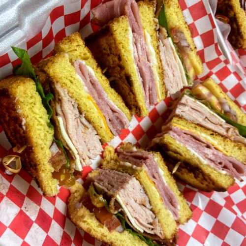 A close-up of stacked sandwiches with layers of meat, cheese, and lettuce on a red and white checkered paper.