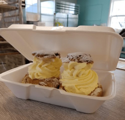 Two cream-filled pastries topped with yellow frosting and powdered sugar, placed in a takeout container.