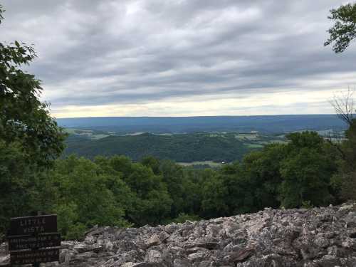 A rocky overlook with a view of rolling green hills and a cloudy sky in the distance. A sign reads "Little Vista."