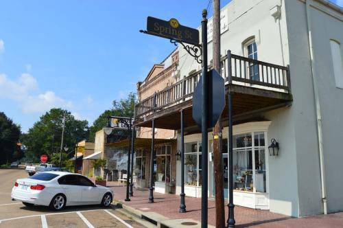 A street view of Spring St, featuring a white car parked and a historic building with a balcony and shops.