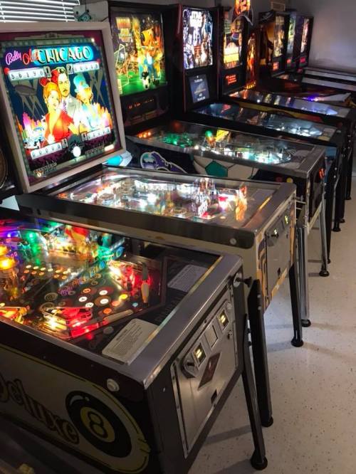 A row of colorful pinball machines with illuminated displays and various themes in a game room setting.
