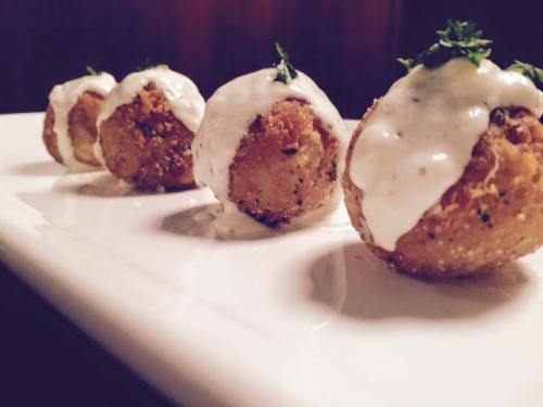 Four crispy balls drizzled with creamy sauce, garnished with herbs, served on a white plate.