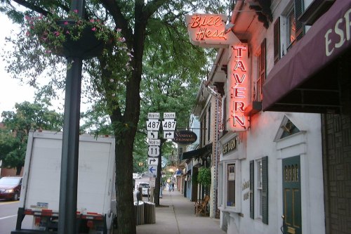 A street view featuring a tavern sign, traffic signs, and trees lining the sidewalk.