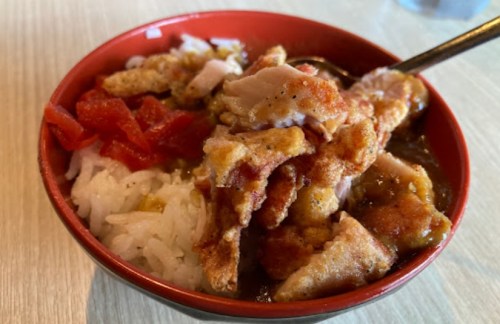 A bowl of rice topped with crispy chicken pieces and diced tomatoes.
