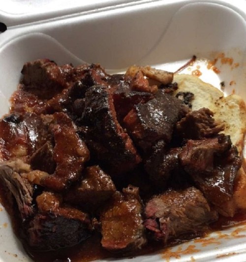 A takeout container filled with pieces of barbecued meat and a slice of bread, coated in sauce.