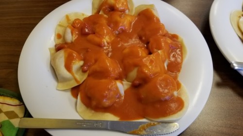 A plate of dumplings topped with a rich tomato sauce, served with a knife on the side.