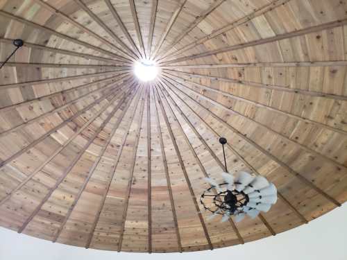 View of a circular wooden ceiling with a central light and a decorative fan hanging below.
