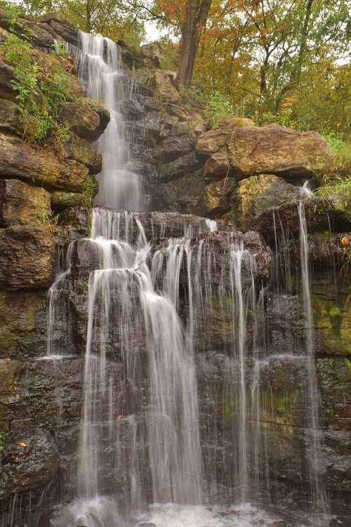 A serene waterfall cascading over rocky terrain, surrounded by lush greenery and autumn foliage.