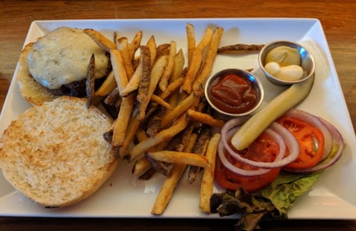 A plate with a burger, fries, pickles, tomato, onion, lettuce, and dipping sauces.