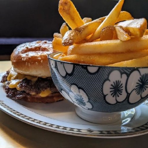 A close-up of a burger with melted cheese next to a bowl of golden French fries on a decorative plate.