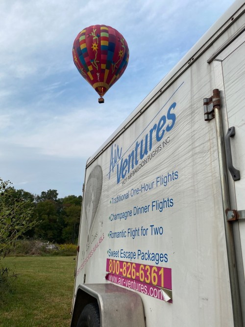A colorful hot air balloon floats above a trailer with "Air Ventures" branding and flight package details.