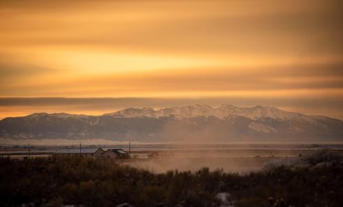 A serene landscape at sunset, featuring mountains in the background and a small house amidst a misty foreground.