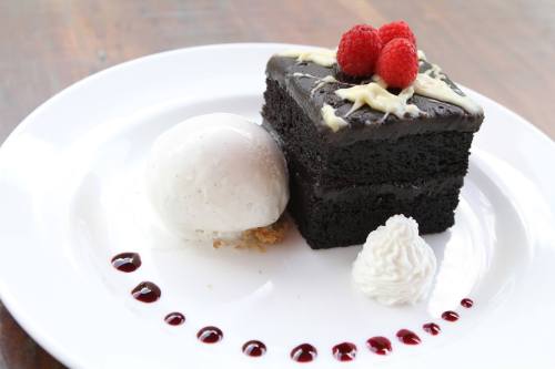 A slice of chocolate cake topped with raspberries, accompanied by a scoop of vanilla ice cream and decorative sauce.