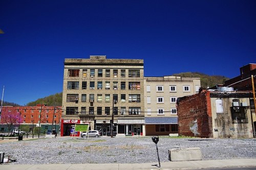 A historic building with a mix of brick and stone, set against a clear blue sky, with a gravel lot in the foreground.