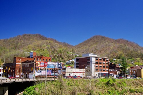 A scenic view of a small town with buildings and billboards, set against green hills under a clear blue sky.