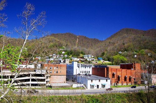 A scenic view of a small town nestled in the mountains, featuring buildings and greenery under a clear blue sky.