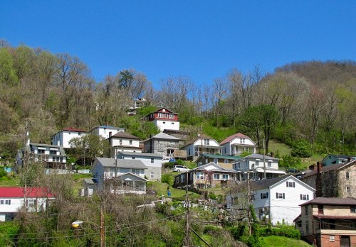 A hillside community with various houses, trees, and a clear blue sky in the background.