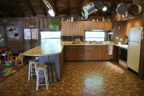 A rustic kitchen with wooden cabinets, a large island, and a cozy atmosphere, featuring a colorful play area in the corner.