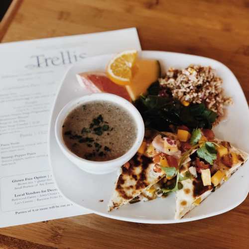 A plate with a slice of quesadilla, salad, fruit, and a bowl of soup, accompanied by a menu in the background.