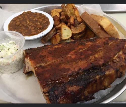 A platter featuring BBQ ribs, baked beans, seasoned potato wedges, coleslaw, and slices of bread.