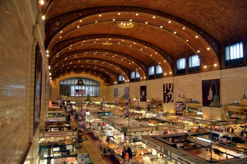 A spacious market hall with arched ceilings, bustling stalls, and warm lighting, showcasing various food vendors.