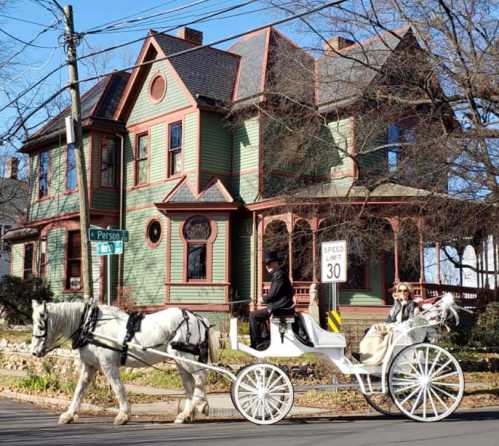 A horse-drawn carriage passes by a colorful Victorian-style house on a sunny day.