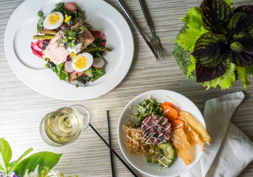 A top-down view of two plates: one with salmon, greens, and eggs; the other with assorted vegetables and a drink.