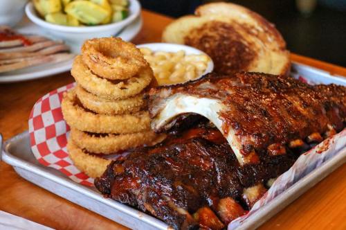 A platter featuring BBQ ribs, onion rings, macaroni and cheese, and toasted bread, served on a checkered tray.