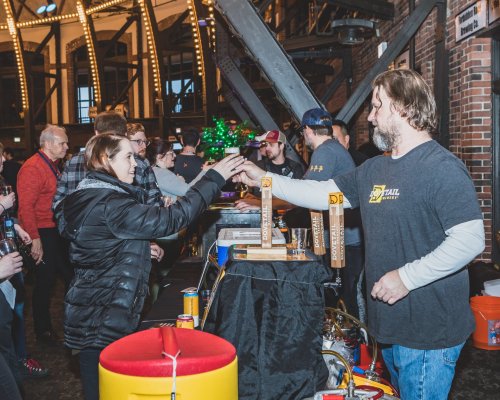 A lively indoor event with people interacting at a bar, serving drinks and enjoying the atmosphere.