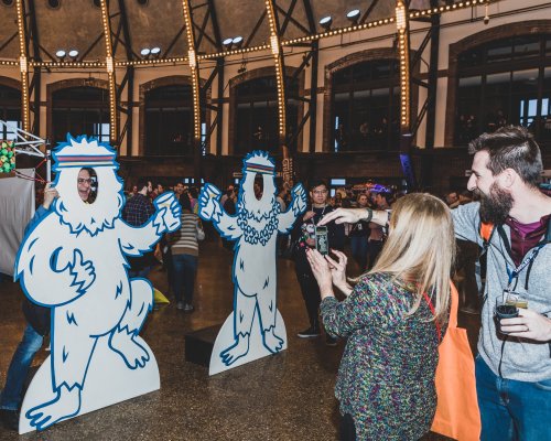 Two large, cartoonish yeti cutouts in a lively indoor event space, with people interacting and enjoying drinks.