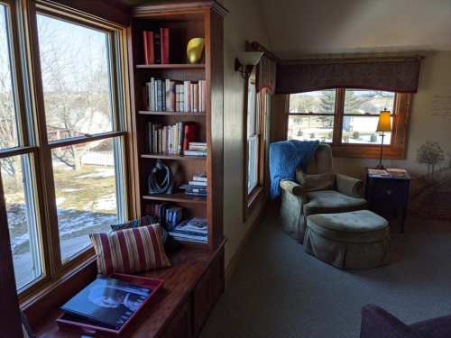 Cozy reading nook with a bookshelf, armchair, and large windows letting in natural light.