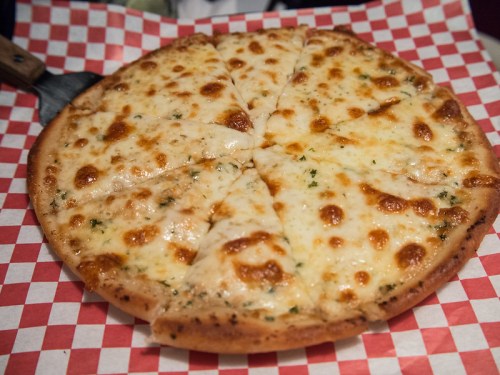 A freshly baked cheese pizza with golden melted cheese, sliced into wedges, on a red and white checkered paper.