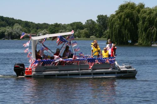A decorated boat with people celebrating on a lake, adorned with American flags and festive attire.