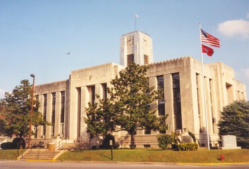 Historic courthouse building with Art Deco architecture, featuring American and Tennessee flags, surrounded by trees.