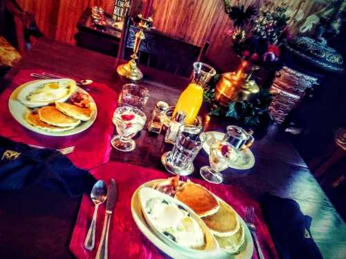 A cozy dining table set with plates of pancakes and eggs, glasses of water, and a colorful drink, surrounded by decor.