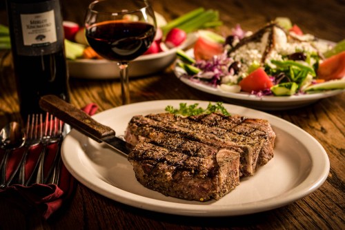 A juicy steak on a plate with a side salad and a glass of red wine in a cozy dining setting.