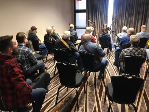 A group of people seated in a room, listening to a musician performing with instruments.