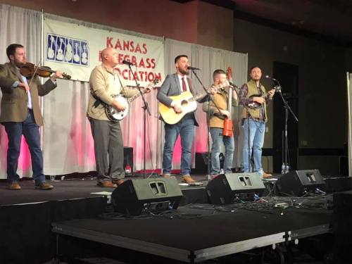 A bluegrass band performs on stage with instruments, including a banjo and guitar, at a Kansas event.