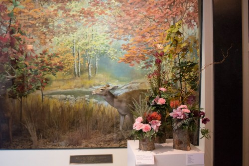 A floral arrangement in front of a colorful nature mural featuring a deer and autumn foliage.