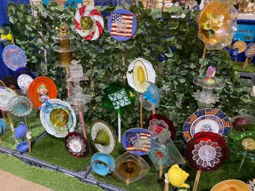 A colorful display of decorative glass plates and garden art arranged among greenery.