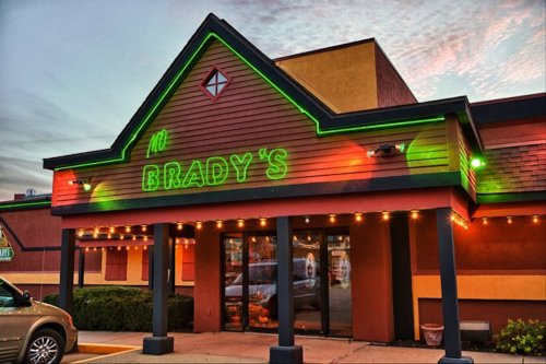 A brightly lit restaurant exterior with a green neon sign reading "Brady's" and colorful lights along the entrance.