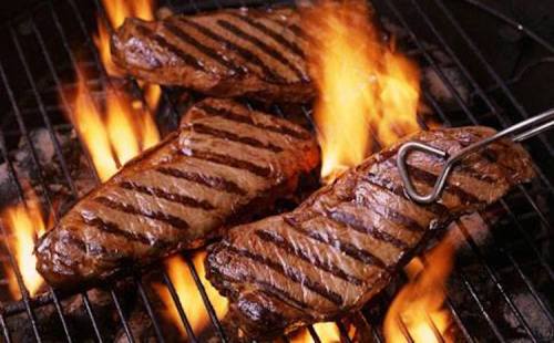 Grilled steaks with grill marks, sizzling over flames on a barbecue.
