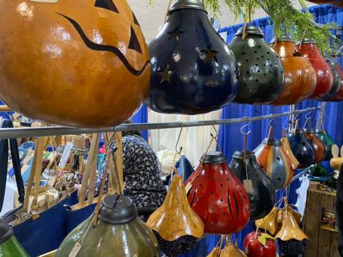 Colorful decorative gourds hang on display, featuring various designs like stars and a jack-o'-lantern face.