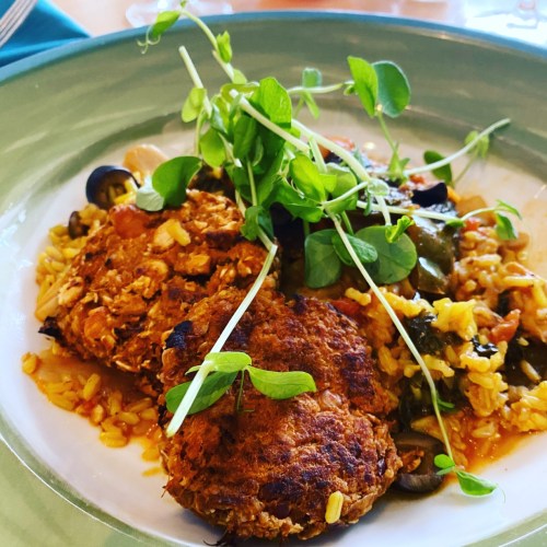 A plate of two golden-brown patties on a bed of rice with vegetables, garnished with fresh pea shoots.