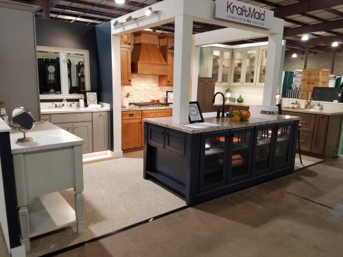 A kitchen display featuring various cabinetry styles, countertops, and a modern sink in a trade show setting.